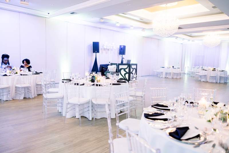 A ballroom set and lit before the guests arrive, white chairs and black napkins