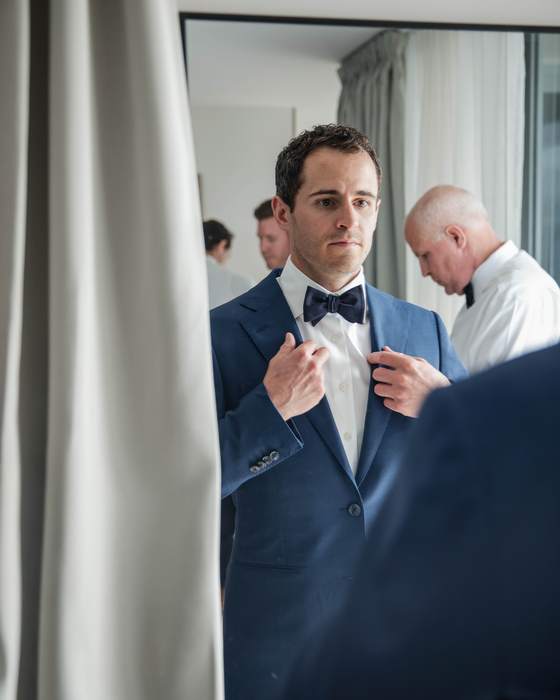 A groom in the mirror as his groomsmen get ready behind him