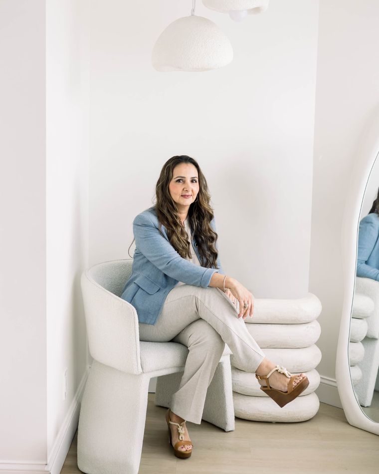 A full length branding portrait of a business owner seated in a boucle chair