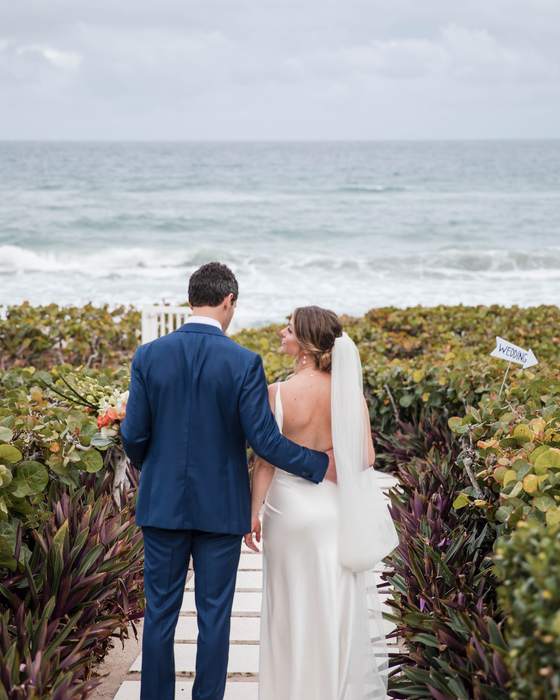 A bride and groom walking a boardwalk toward the sea