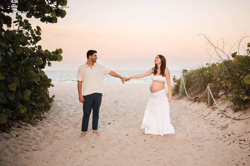 An expecting couple walking a beach path at golden hour