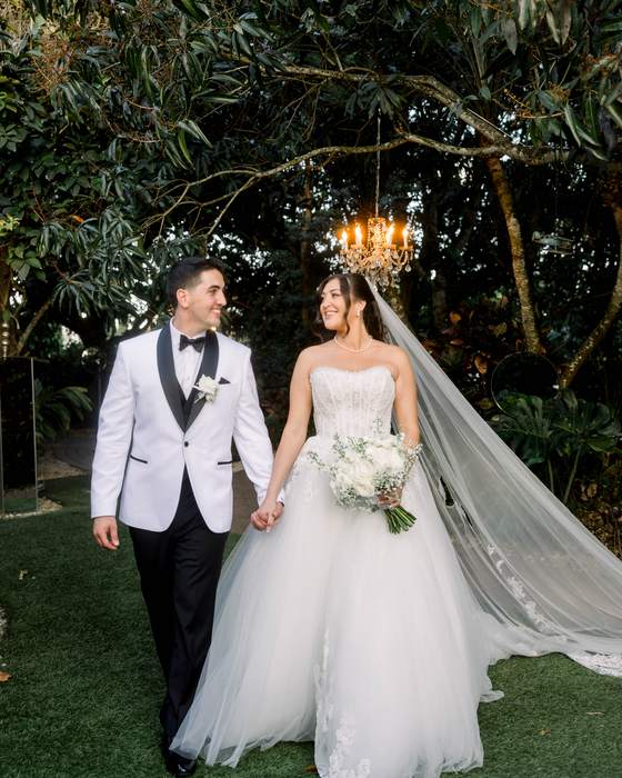 A bride and groom beneath a chandelier hung in a tree at dusk