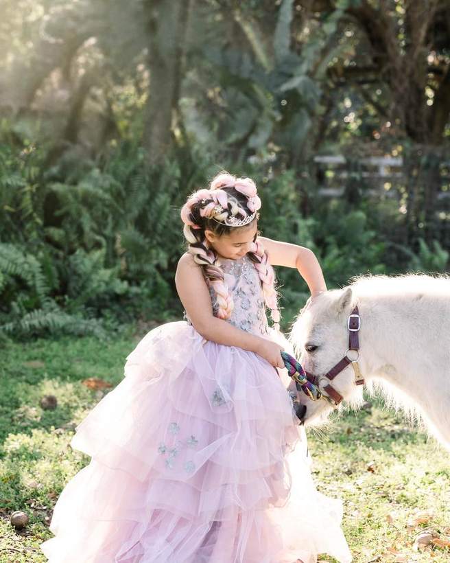 A child in a tulle gown with a pony under a flowering tree