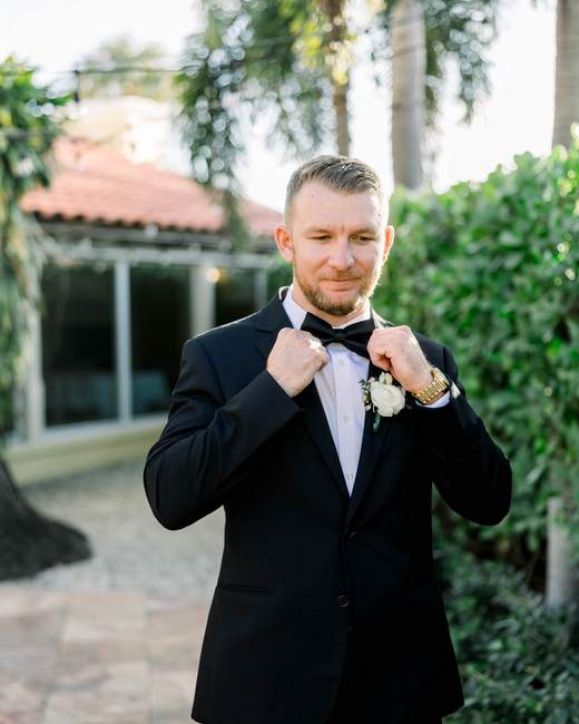 A groom fixing his bow tie in a garden before the ceremony