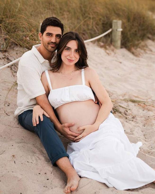 An expecting couple on the sand at sunset