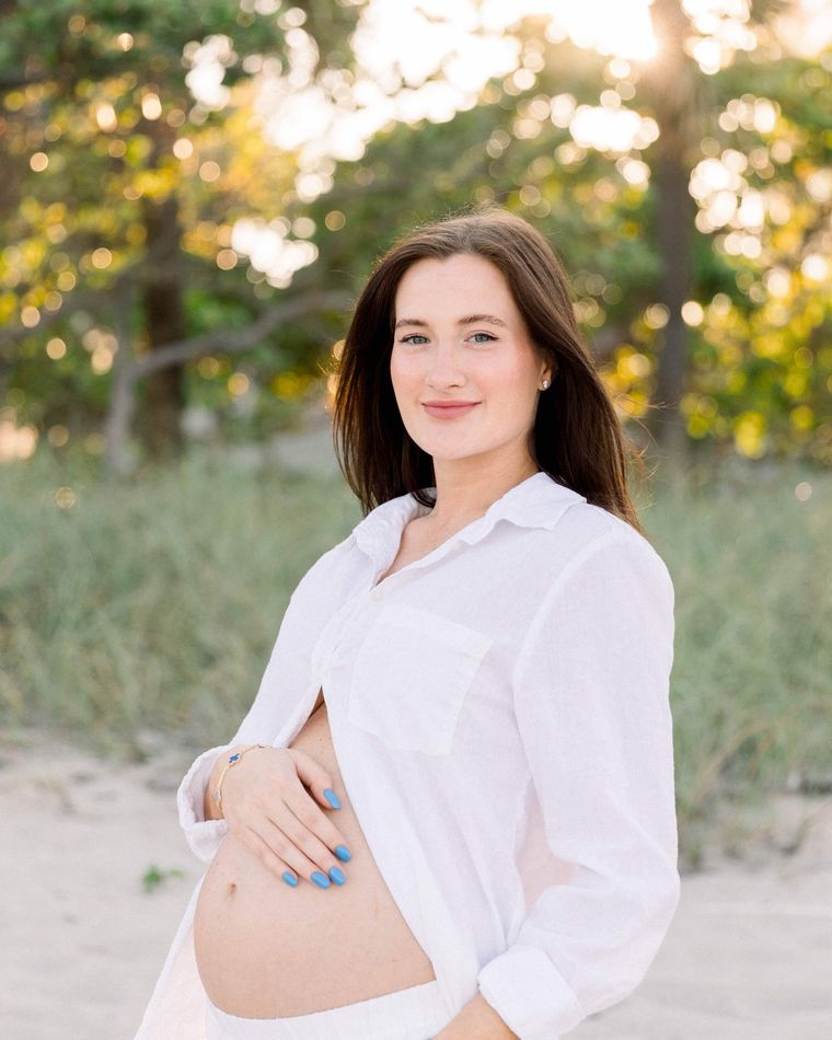 An expecting mother resting a hand on her bump, beach grass behind her