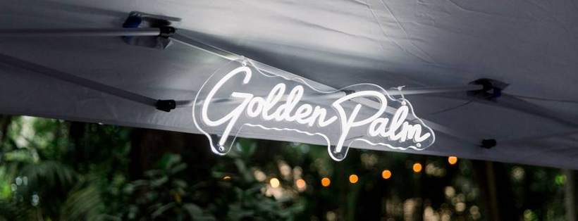 The Golden Palm neon sign hanging in a photobooth canopy at dusk