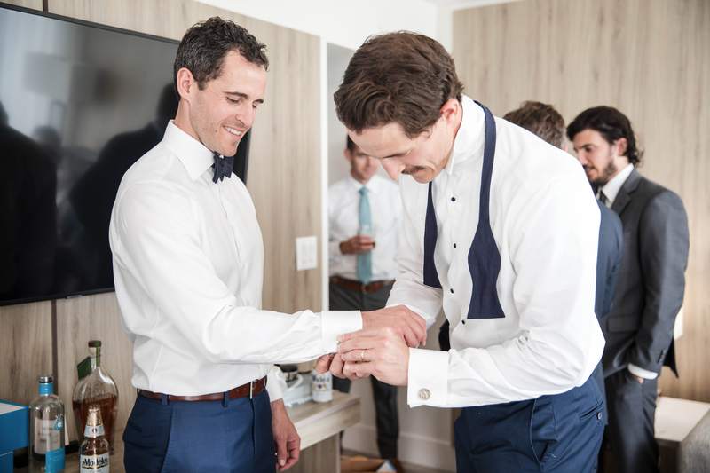 A groomsman fastening the groom's cufflink before the ceremony