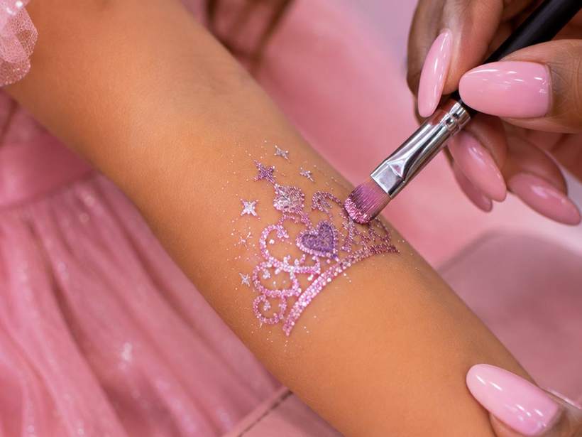 A glitter tiara tattoo being painted onto a guest's arm