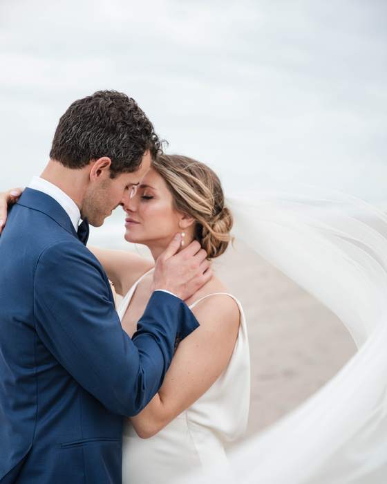 A bride and groom on the sand, her veil sweeping across them