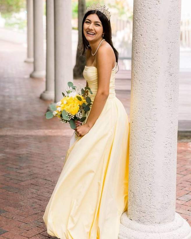 A quinceanera in a yellow gown against the columns