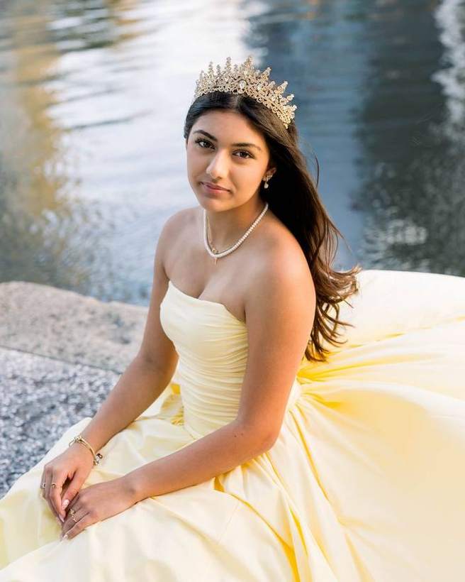 A quinceanera seated by the water in her crown