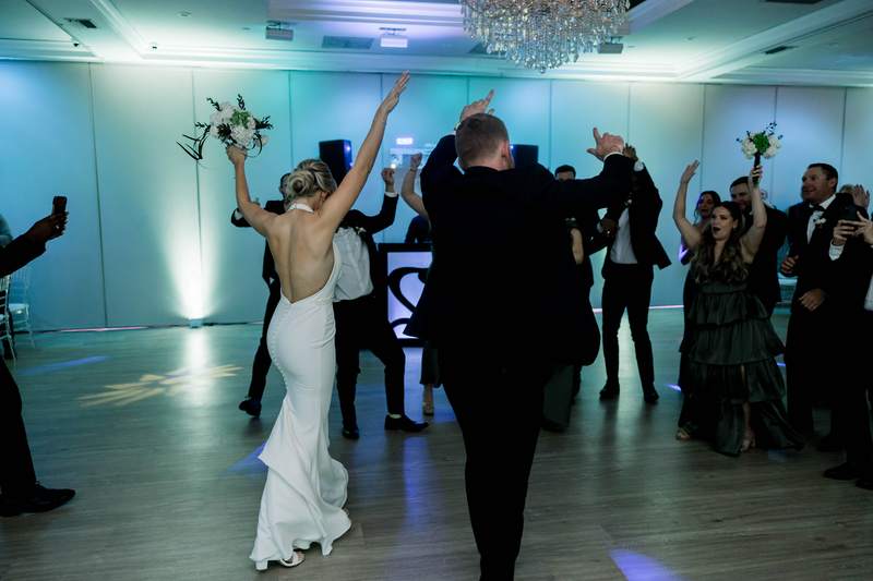 A bride with her arms up on the dance floor, guests around her
