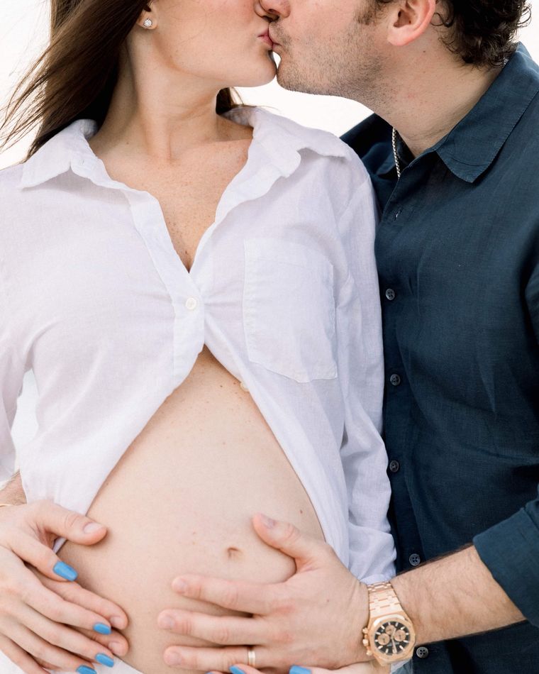 An expecting couple kissing, both hands held over her bump