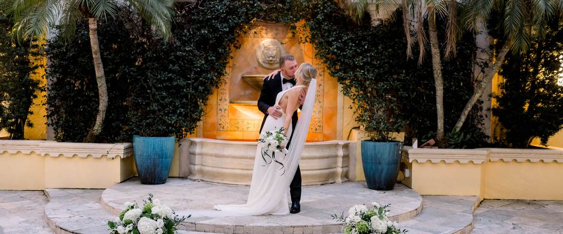 A wedding ceremony at a stone fountain in golden light, framed by ivy and palms